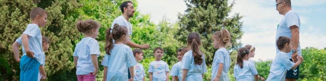 Group of children and teachers playing and learning in a sunny park setting.