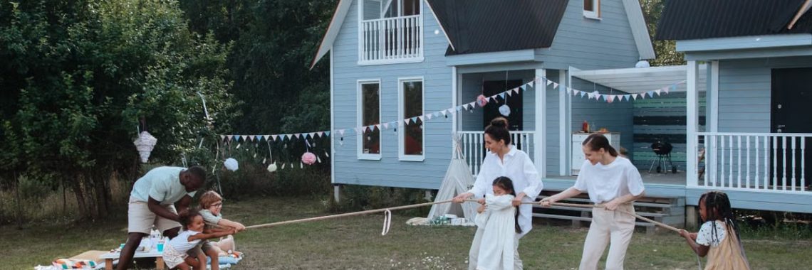 Happy family playing tug of war in front of cozy houses during a summer day.