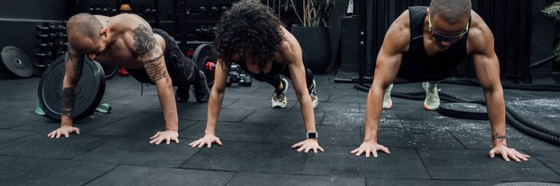 Three individuals performing push-ups together in a Mexico City gym setting.